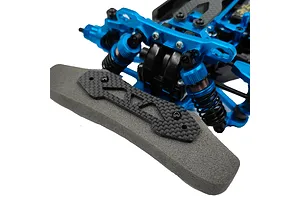 Close-up of a carbon fibre bumper plate installed on the front of a blue anodized RC car chassis with a grey foam bumper.