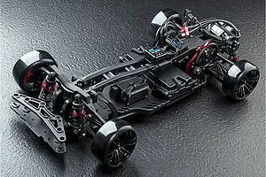 High-angle studio shot of an MST RMX 2.5 RC drift car chassis, showing the black plastic frame, suspension components, and drift tires on a textured surface.
