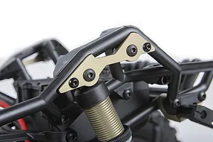 Close-up of gold-coloured aluminium shock mount plates installed on a black RC vehicle chassis frame.