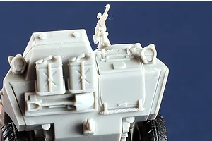 Close-up of an unpainted grey plastic model of an M706 Commando armoured car showing the rear deck with jerry cans, a shovel, and a mounted machine gun.