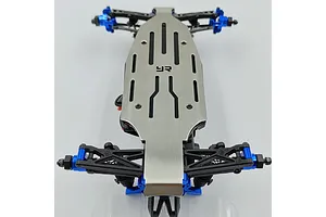 A Yeah Racing stainless steel chassis skid plate installed on the underside of an RC car chassis with blue aluminum components.