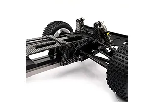 Close-up of an RC car chassis featuring black carbon fiber plates, metal shock absorbers, and off-road tires against a white background.