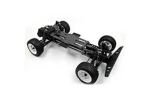 A high-angle studio shot of an assembled RC car chassis featuring a carbon fiber deck, black plastic components, and white wheels with off-road tires.