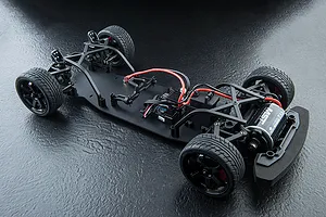 Top-down view of an MST TCR-FF RC car chassis without the body shell, showing the motor, electronics, and wheels on a black textured surface.