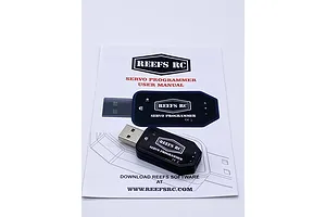 A Reefs RC USB servo programmer device resting on top of its printed user manual.