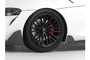 Close-up of the front wheel and fender of a white Tamiya 1/24 Toyota GR Supra scale model car featuring black TRD rims and red brake calipers.