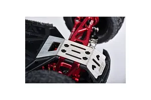 A stainless steel skid plate installed on the underside of an RC car chassis, showing red aluminum suspension components and black tires.