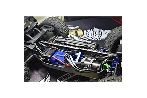 Close-up of an RC car chassis showing a carbon fibre T-bar brace installed over the central drivetrain components.