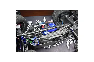 A close-up view of an RC car chassis featuring a carbon fibre T-bar brace installed over the central drivetrain components.