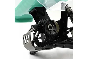 Close-up of a black aluminium motor mount and gear assembly installed on an RC car chassis with a teal wing visible in the background.