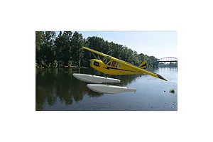 A yellow RC floatplane flying over a river in a digital simulation environment.