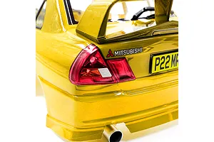 Close-up of the rear section of a yellow RC Mitsubishi Lancer Evo IV body shell, showing the tail light, spoiler, and exhaust pipe.