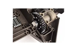 A black spur gear installed in the chassis of an RC vehicle, showing the gear mesh and mounting hub.