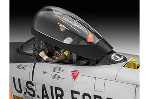 Close-up of a 1/48 scale F-86D Dog Sabre model cockpit with pilot figure, open canopy, and detailed warning decals on the silver fuselage.