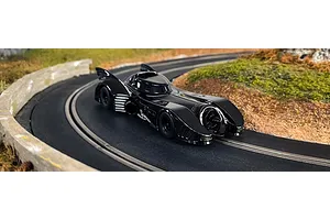 A black 1989 Batmobile slot car driving on a curved Scalextric track with a grassy landscape background.