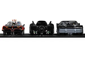 Three Scalextric Batmobile slot cars lined up on a black track, including the 1966, 1989, and The Batman versions.
