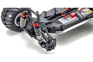 Close-up of the front suspension and chassis of a Kyosho Mad Van RC truck, showing red shocks, black plastic arms, and a battery pack.