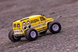 A yellow Kyosho Mad Van RC monster truck with Mooneyes branding driving on a gravel surface.