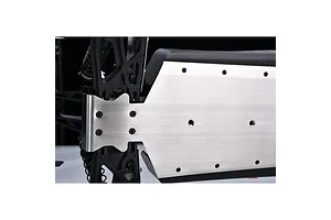 A close-up view of a silver stainless steel chassis skid plate installed on the underside of an RC vehicle, showing mounting screws and black plastic suspension components.