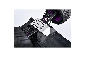 A silver GPM stainless steel skid plate installed on the front chassis of an RC monster truck with black suspension arms and purple springs.