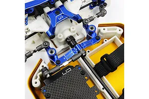 Close-up of a blue anodized aluminium steering assembly installed on an RC car chassis with white plastic and carbon fiber components.