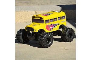 A yellow Pro-Line RC school bus body shell mounted on a monster truck chassis, featuring flame decals and black off-road tires on a concrete surface.