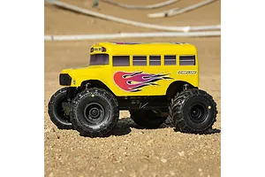 A yellow Pro-Line school bus RC body shell mounted on a monster truck chassis, sitting on a dirt track.