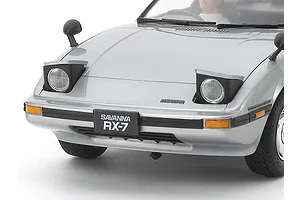 Close-up of a silver Tamiya 1/24 scale Mazda Savanna RX-7 model car showing the front bumper, pop-up headlights, and license plate.