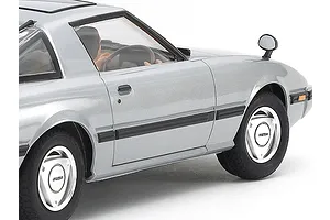 Close-up side view of a silver Tamiya 1/24 scale Mazda Savanna RX-7 plastic model car showing the driver figure, wheels, and body details.
