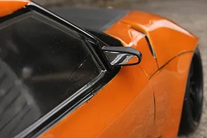 Close-up of a black aero door mirror mounted on an orange RC car body shell.