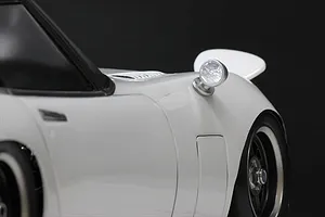 A close-up view of a white RC car body shell featuring a classic round fender-mounted side mirror.