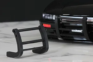 A black 1/10 scale RC grill guard sitting on a white marble surface in front of a black RC car body shell.