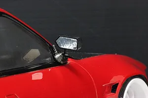 Close-up of a black racing-style side mirror mounted on a red RC car body shell.