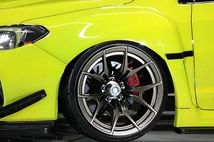Close-up of a lime green RC car wheel showing a bronze multi-spoke rim and a red brake caliper installed behind it.