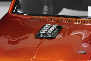 A close-up of a metallic orange RC car hood featuring a black intake manifold with eight silver velocity stacks installed.