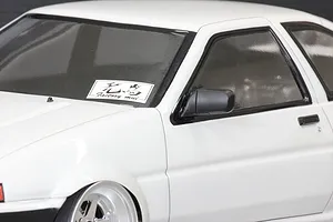 Close-up of a white 1/10 scale RC AE86 body shell featuring a black side mirror and a Factory mui sticker on the windshield.