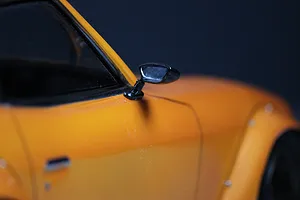 A close-up view of a black side mirror mounted on the orange body shell of a 1/10 scale RC car.
