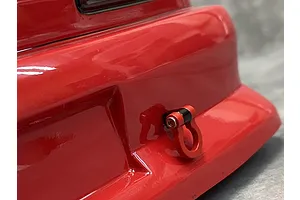 A red RC car tow hook accessory installed on the rear bumper of a glossy red RC car body shell.