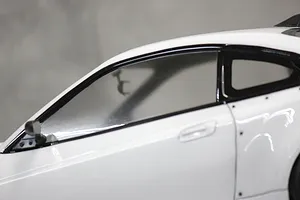 Close-up of a white RC car body shell showing the side window, door handle, and a small black side mirror attached to the door frame.