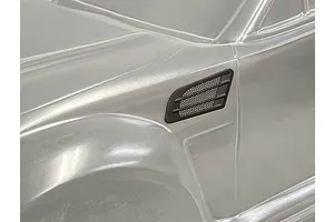 A black plastic fender duct accessory installed on a clear, unpainted 1/10 scale RC car body shell.