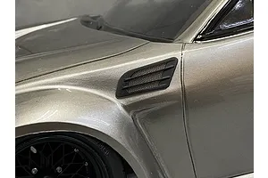 A close-up view of a black fender duct accessory installed on the side of a metallic silver RC car body shell.