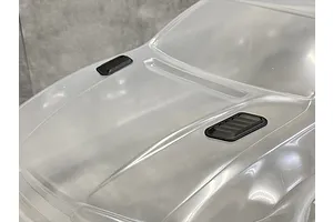 A close-up view of two black plastic bonnet ducts installed on a clear, unpainted 1/10 scale RC car body shell.