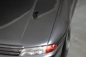 A close-up view of a dark grey RC car body shell featuring a small black NACA duct installed on the hood.