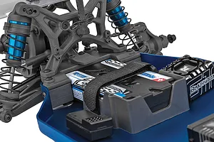 Close-up of the chassis of a Team Associated RC buggy showing the battery, blue shock absorbers, and electronic speed controller.