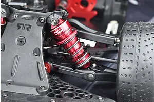 A close-up view of a red GPM Racing aluminium shock absorber installed on the front suspension of an RC car.