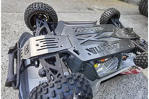 Underside view of an RC vehicle showing a GPM stainless steel chassis skid plate installed on an Arrma chassis.
