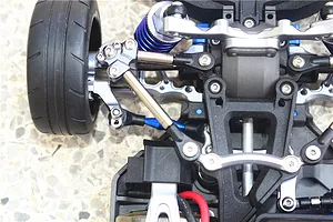 Close-up of an RC car front suspension assembly featuring GPM titanium tie rods and blue aluminium components installed on a chassis.