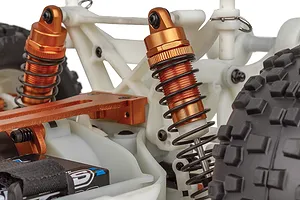 Close-up of the orange anodized shock absorbers and white plastic chassis components on a Team Associated Rival MT10 RC monster truck.