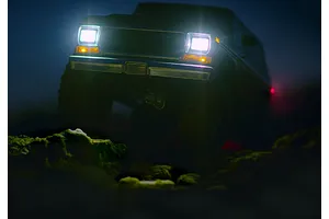A dark, low-angle shot of an RC truck driving over rocks at night, with its bright LED headlights illuminated.