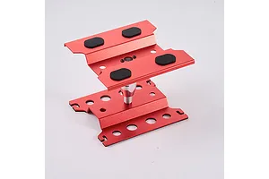 A red anodized aluminium RC car maintenance stand with black rubber pads on a white background.